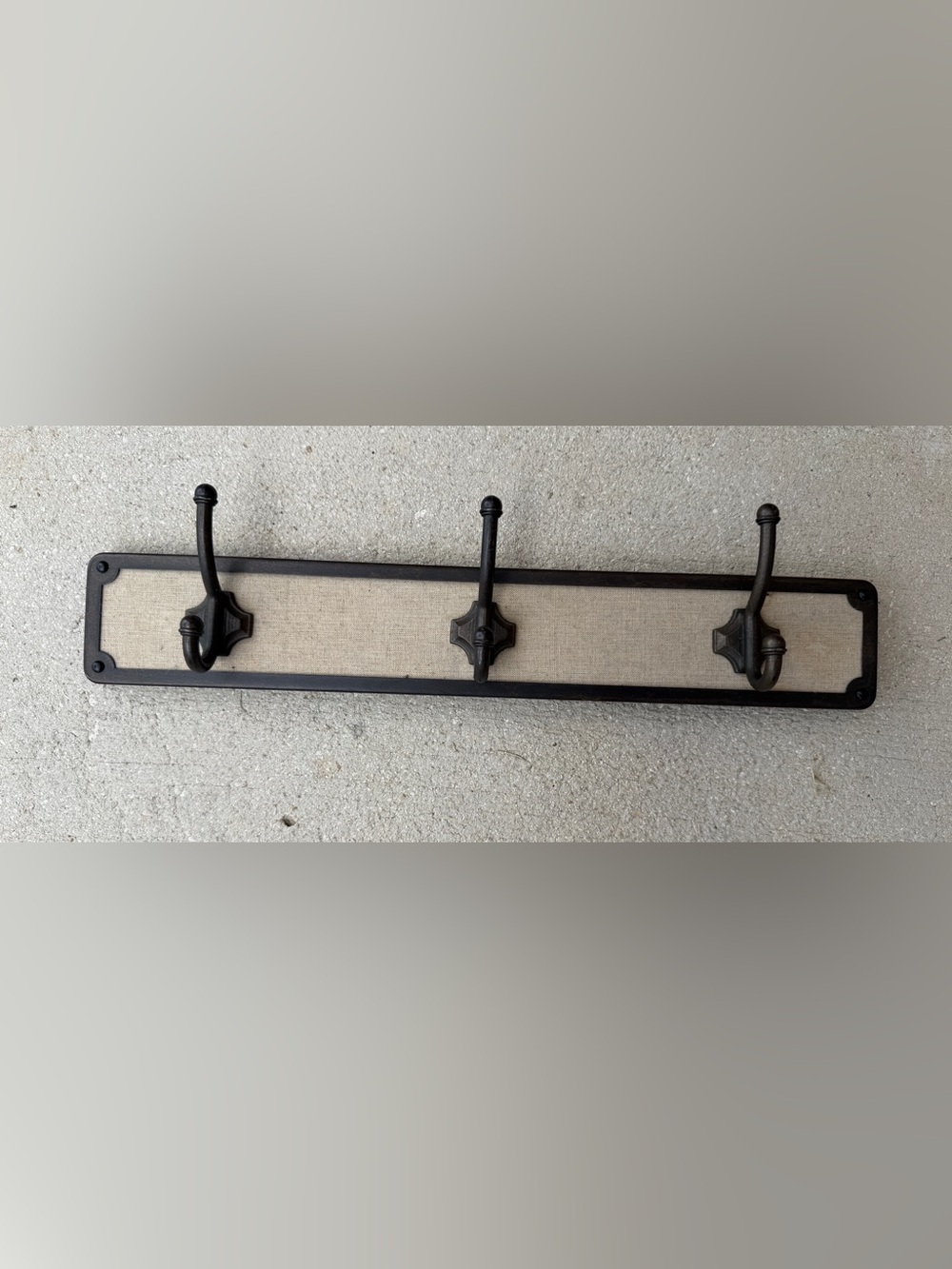Hook rack features a dark bronze frame with a light-colored linen backing